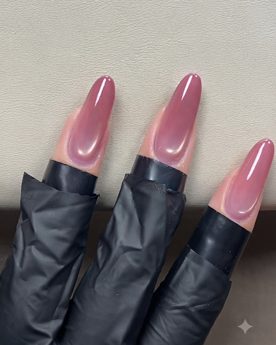 Un pennellino che stende un top coat trasparente su unghie a mandorla cat-eye per una finitura lucida.