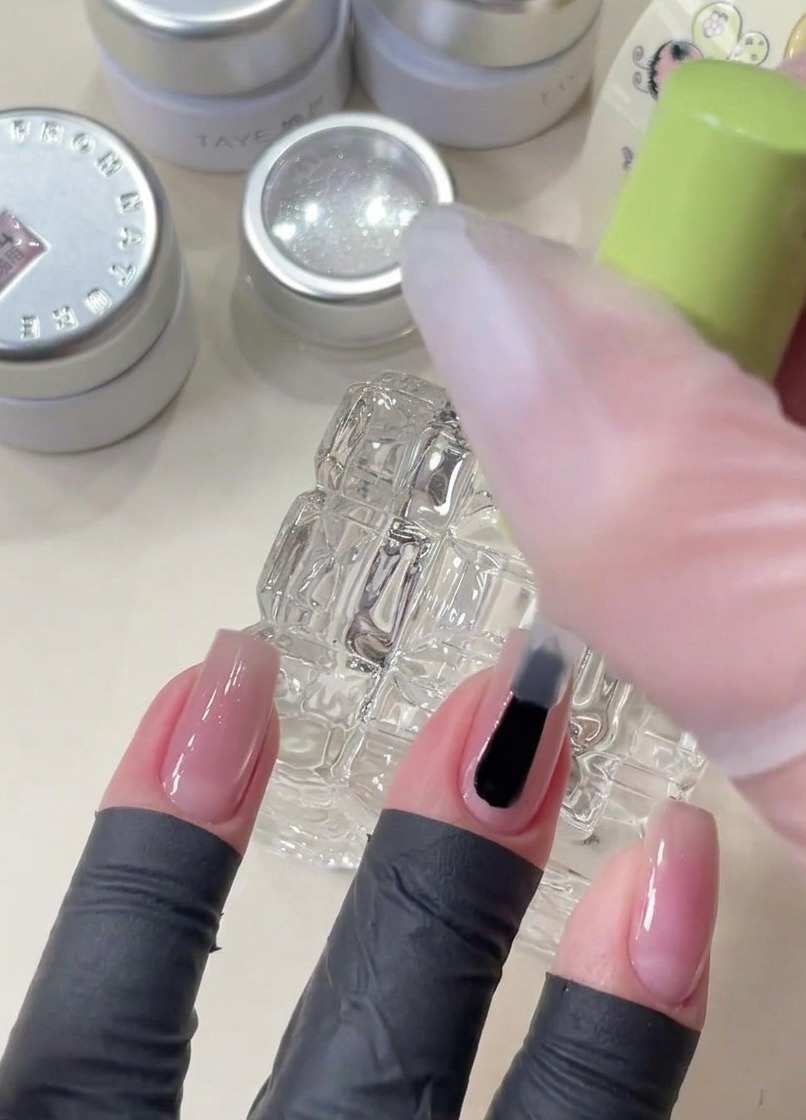 Un pennello che applica il gel base trasparente su ununghia prima di posizionare le paillettes decorative a stella.