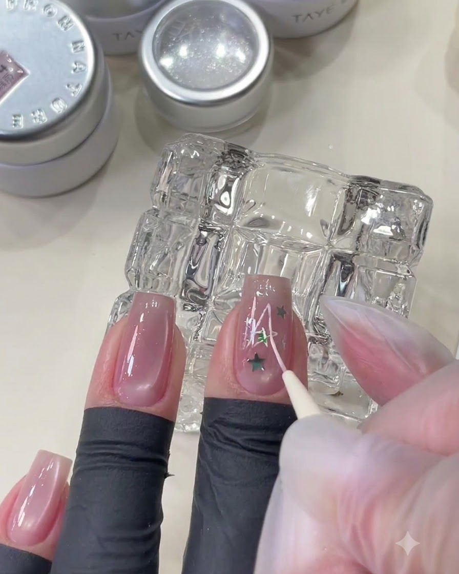 Un pennello liner fine che disegna un design di stella rosa sopra ununghia adornata con paillettes a stella.