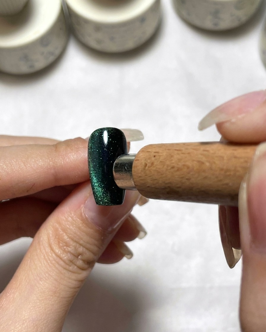 Uno strumento magnetico posizionato accanto a ununghia cat eye verde scuro per distribuire il pigmento.