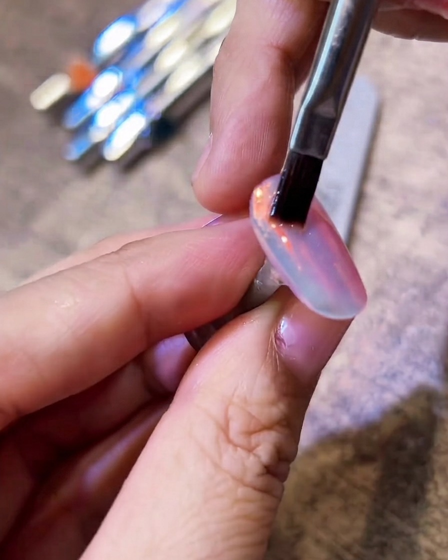 Un pennello a setole piatte che passa delicatamente su ununghia brillante cromo aurora per rimuovere la polvere in eccesso.