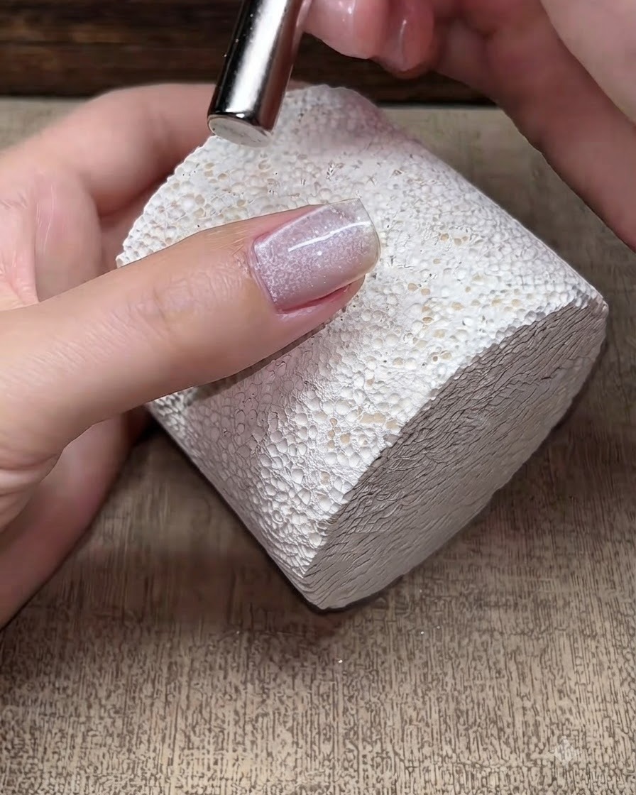 Un piccolo magnete che si libra sopra ununghia con gel cat-eye fresco per manipolare le particelle di shimmer magnetico.