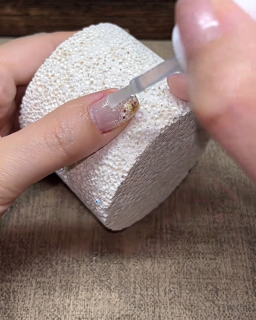 Un pennello che applica uno strato trasparente di builder gel su una superficie ungueale decorata.