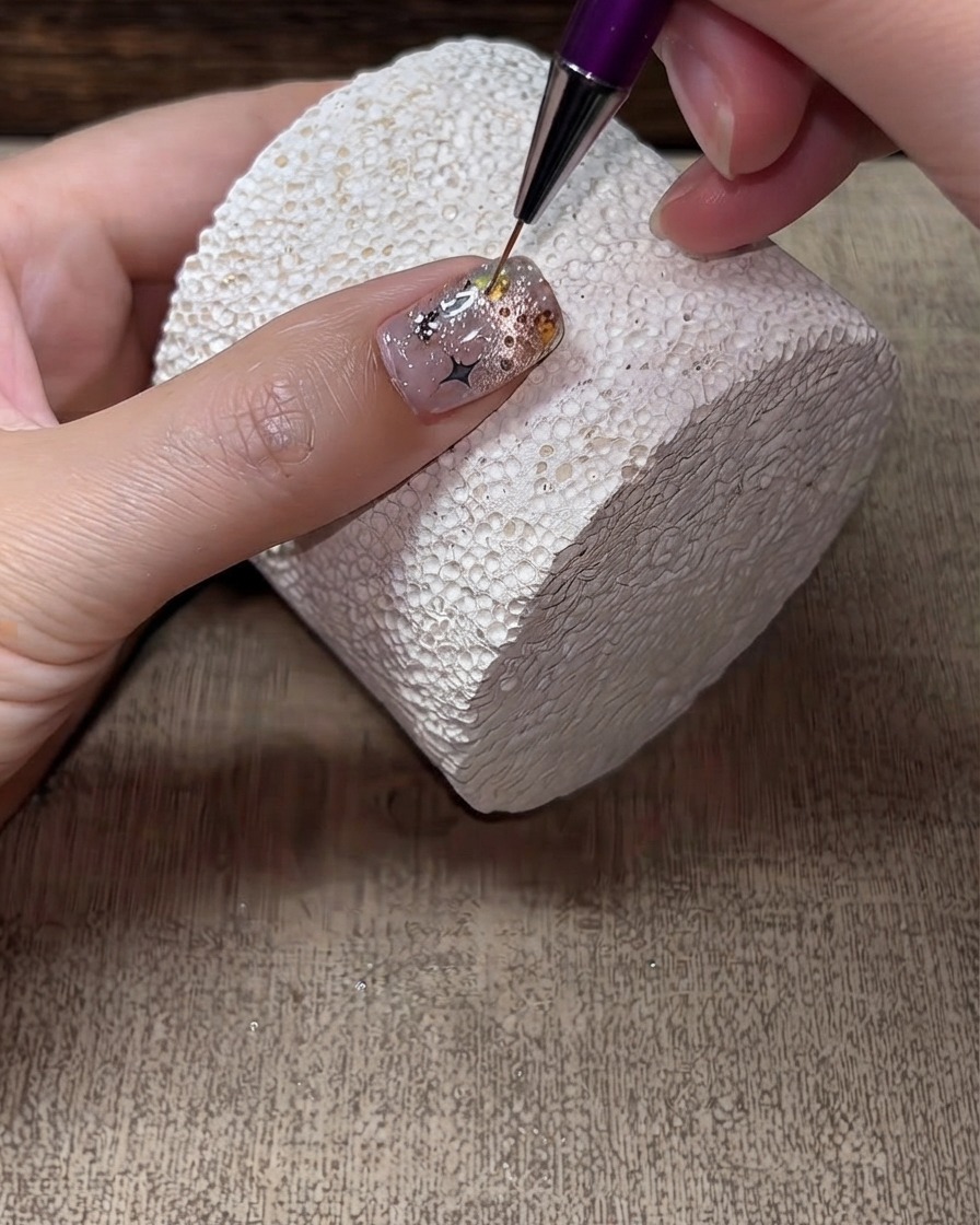 Un pennello liner sottile che applica il top coat duro attorno ai bordi e agli spazi vuoti degli strass su ununghia finita.