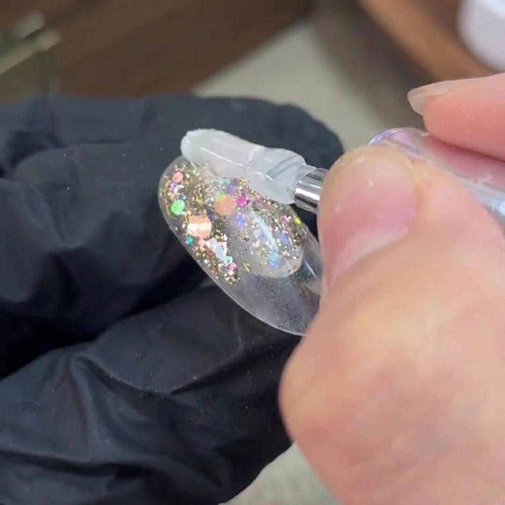 Un pennello che applica il gel base trasparente su uno strato di glitter polimerizzato su ununghia.
