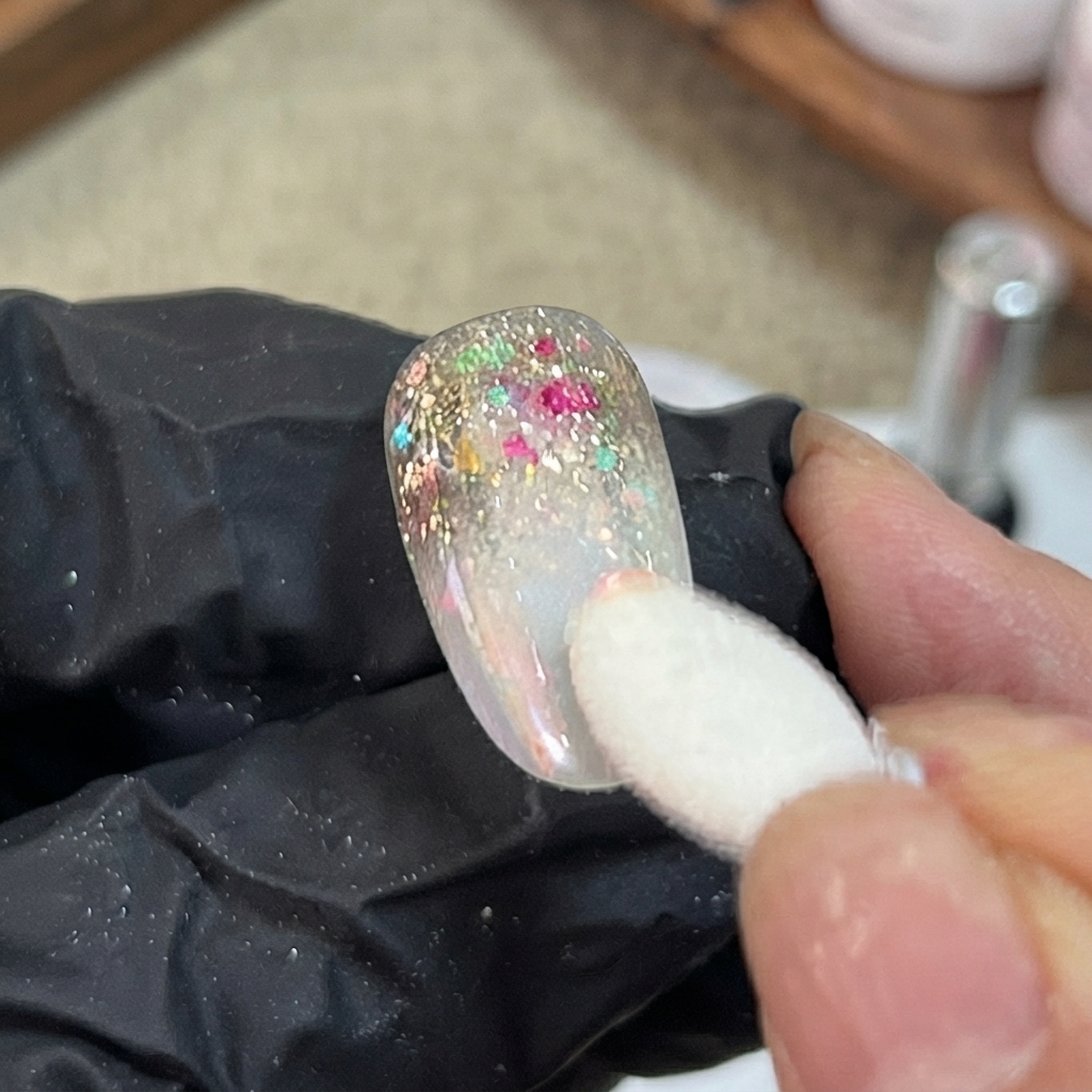 Un applicatore in spugna che tampona la polvere aurora iridescente sulla sezione sfumata di ununghia artificiale decorata.