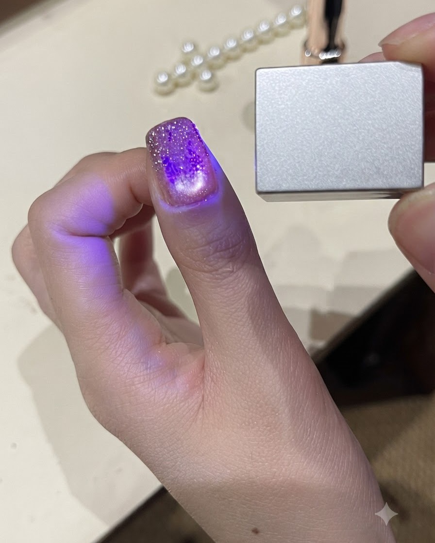 Una vista ravvicinata di un pollice sotto una piccola luce LED UV portatile che polimerizza lo smalto gel.