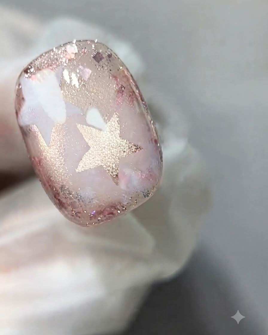 Un pennello per unghie che applica uno strato di gel cat-eye rosa trasparente sulla superficie di ununghia decorata.