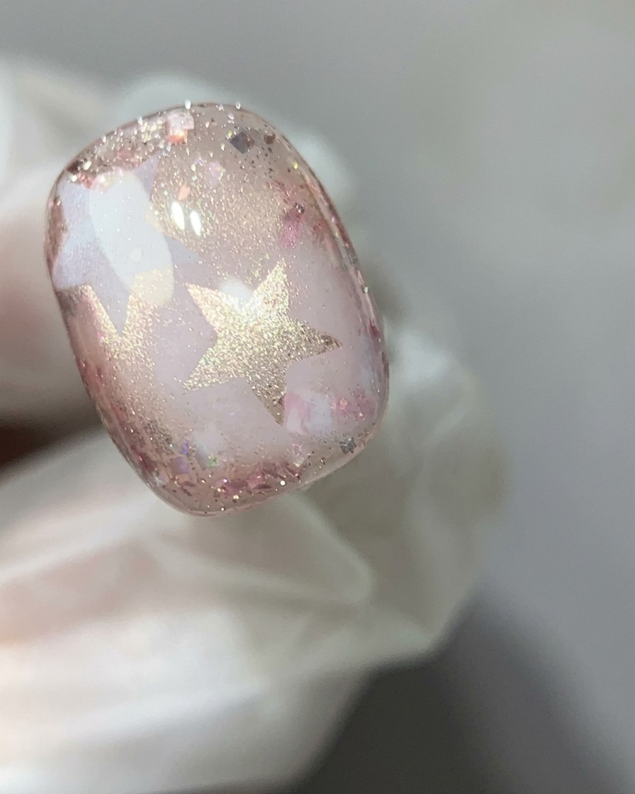 Una bacchetta magnetica tenuta sopra ununghia in gel cat-eye rosa per concentrare il riflesso luccicante in un effetto perla di vetro.
