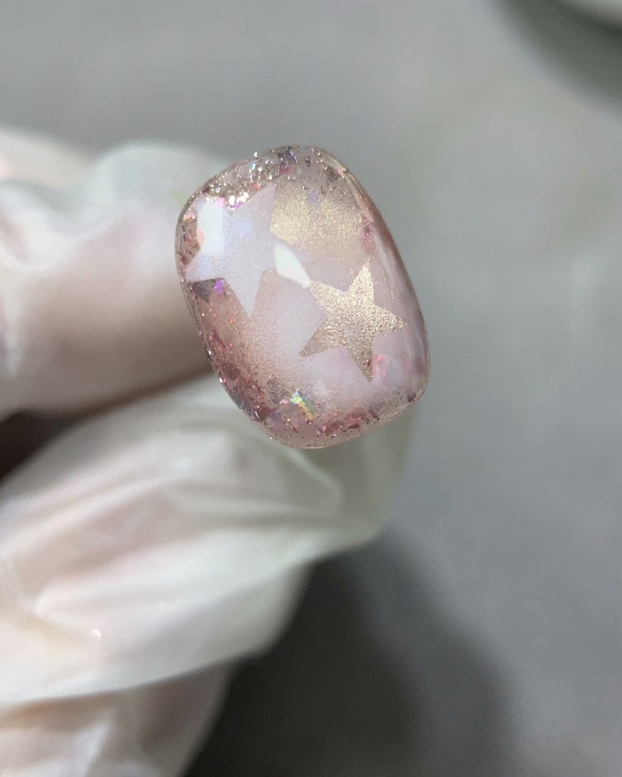 Un pennello per unghie che stende uno strato sottile e liscio di base gel trasparente sul design completo con stella e glitter.