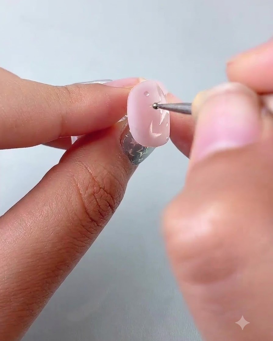 Un dotting pen che posiziona piccoli pois di accento attorno alle stelle dipinte su ununghia rosa.