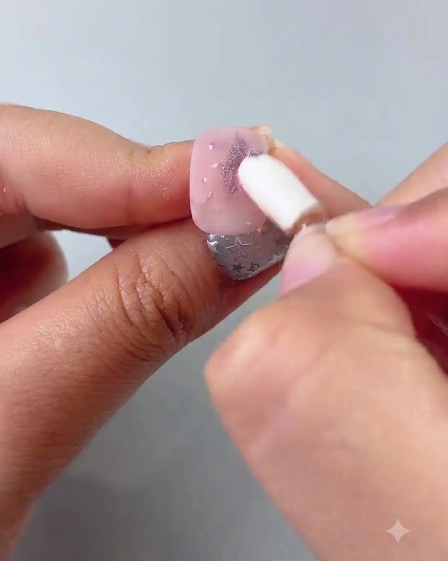 Un applicatore in spugna di silicone che strofina la polvere cromata viola sulle stelle dipinte su ununghia.