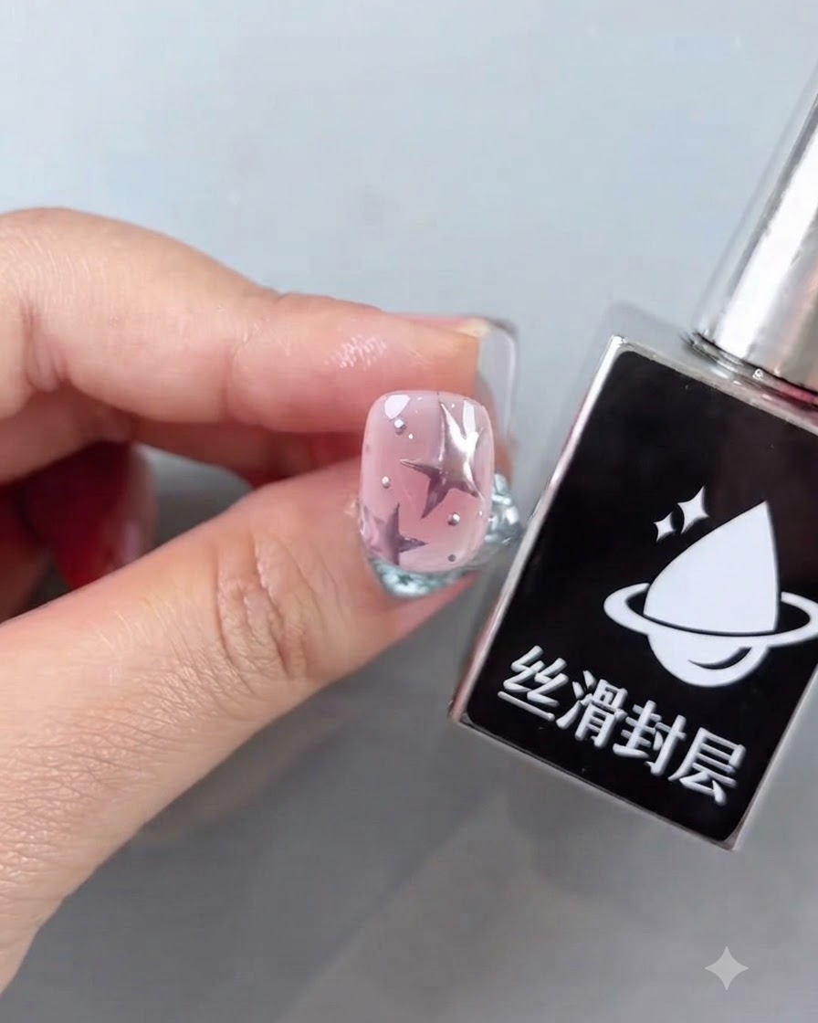 Una boccetta di top coat liscio accanto a ununghia rosa finita con disegni di stelle e accenti argentati lucidi.