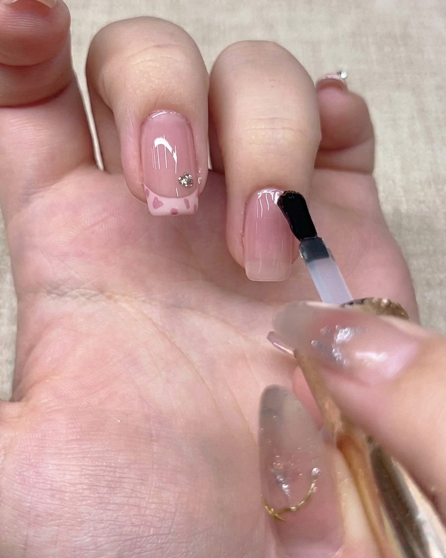 Un pennello applica un top coat trasparente sullunghia del dito anulare.