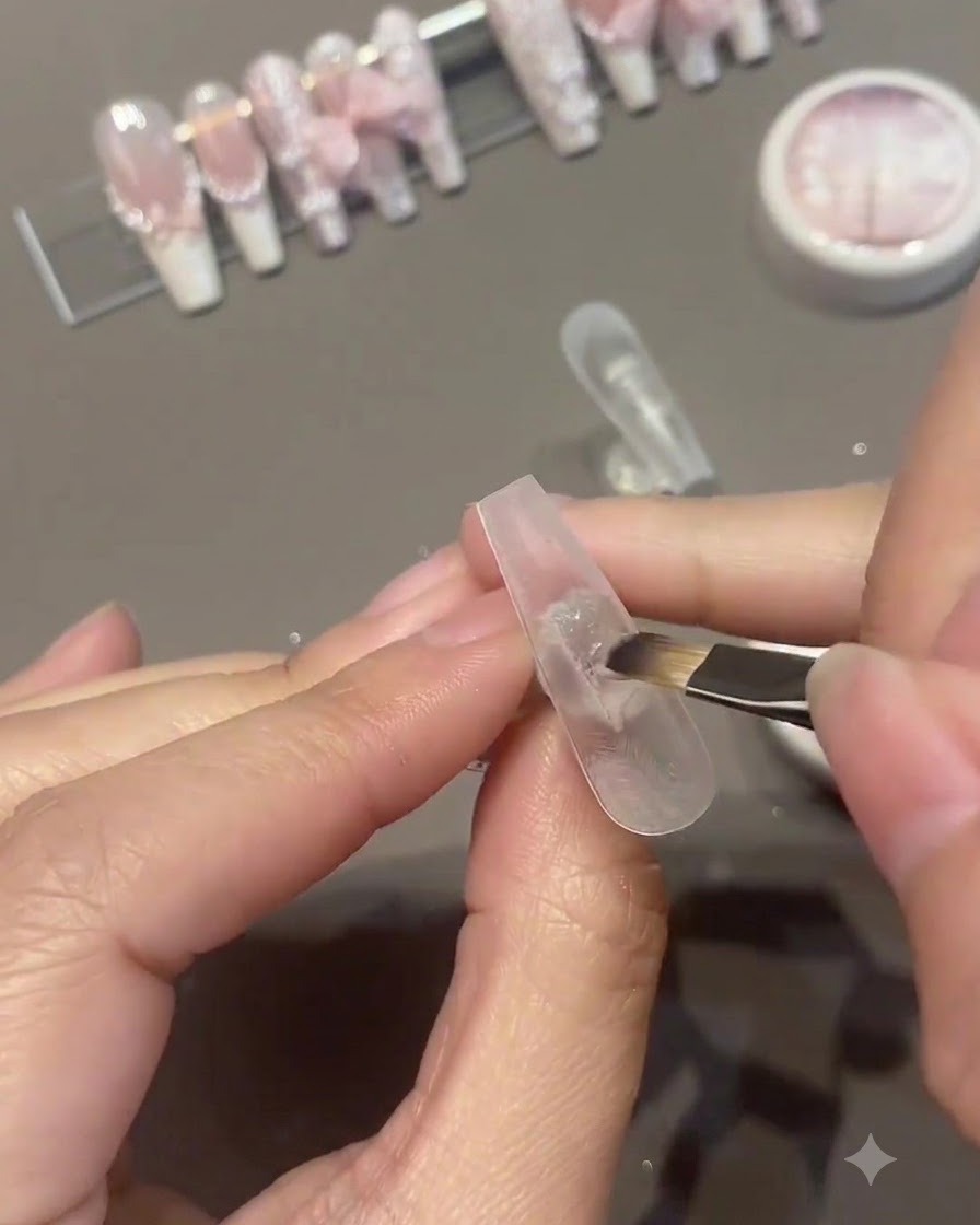 Un pennello che applica una seconda mano di smalto gel rosa sulla superficie di ununghia artificiale.