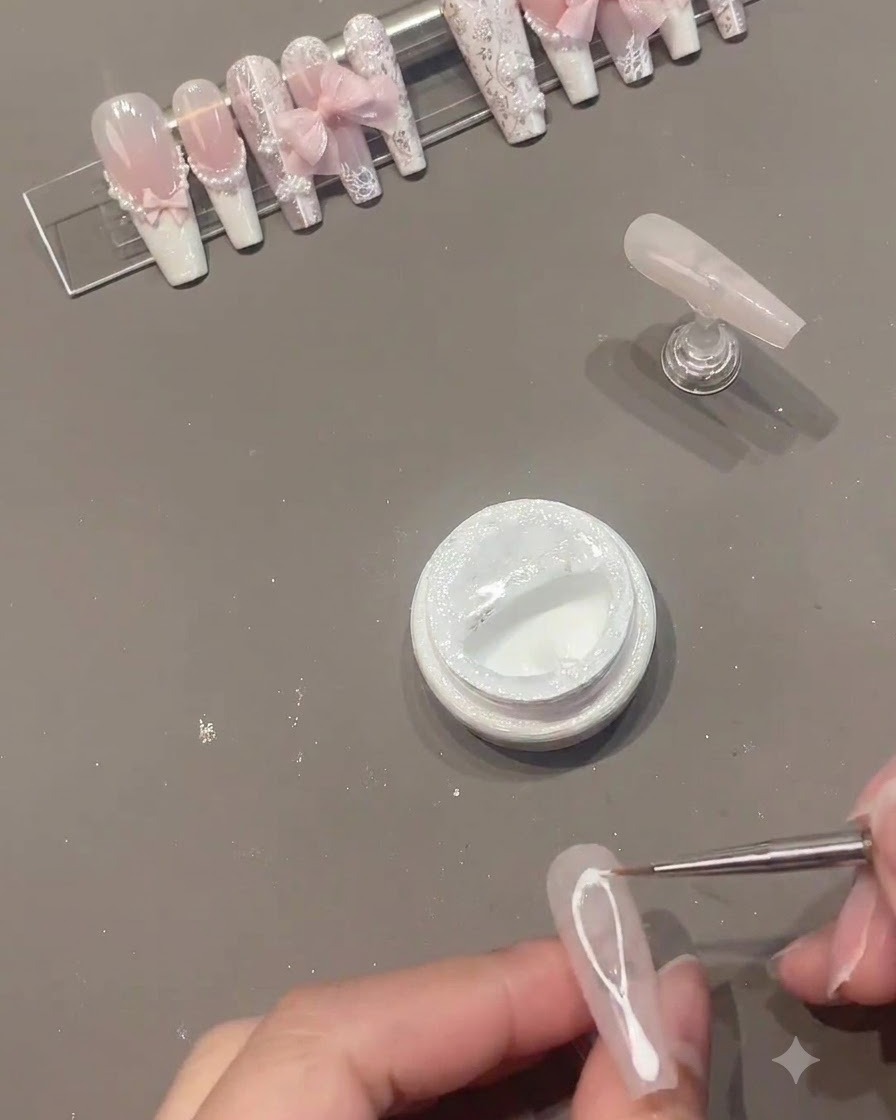 Un pennello sottile che disegna linee in gel spider bianco al centro di ununghia in gel rosa.