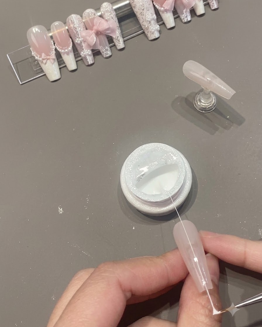 Un sottile filo di gel spider bianco tirato attraverso la superficie dellunghia sopra un barattolo aperto.
