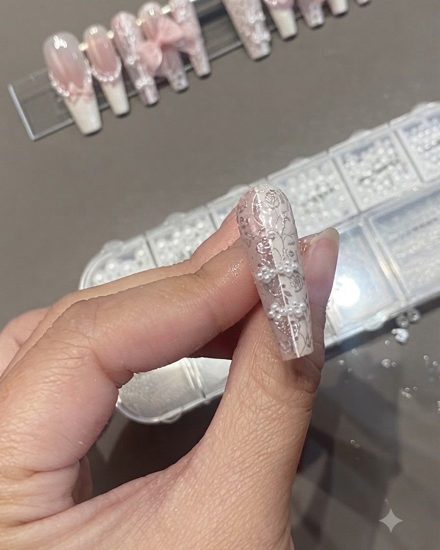 Un pennello per unghie che applica un top coat trasparente su un design per unghie strutturato con perle e stamping in pizzo.