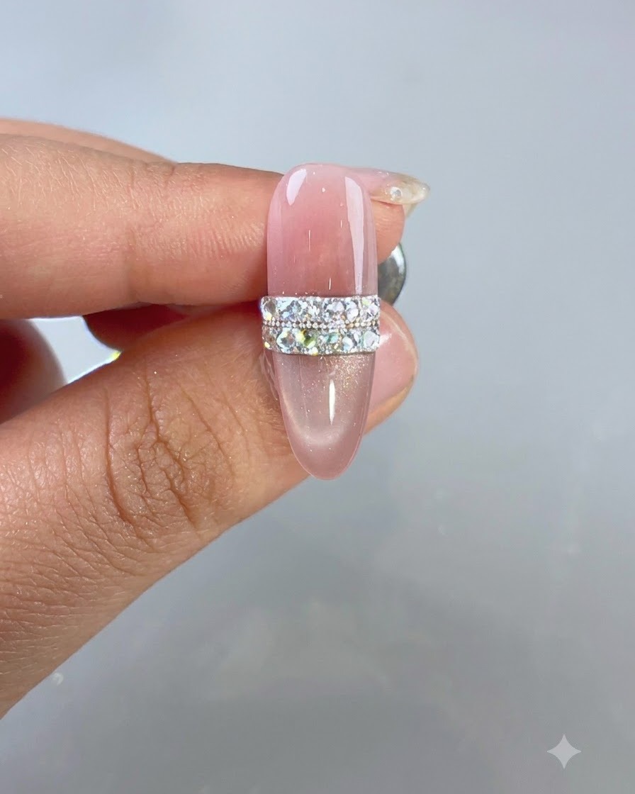 Un design per unghie cat-eye rosa completato con un motivo ad anello di strass e perle scintillanti sotto la luce dello studio.
