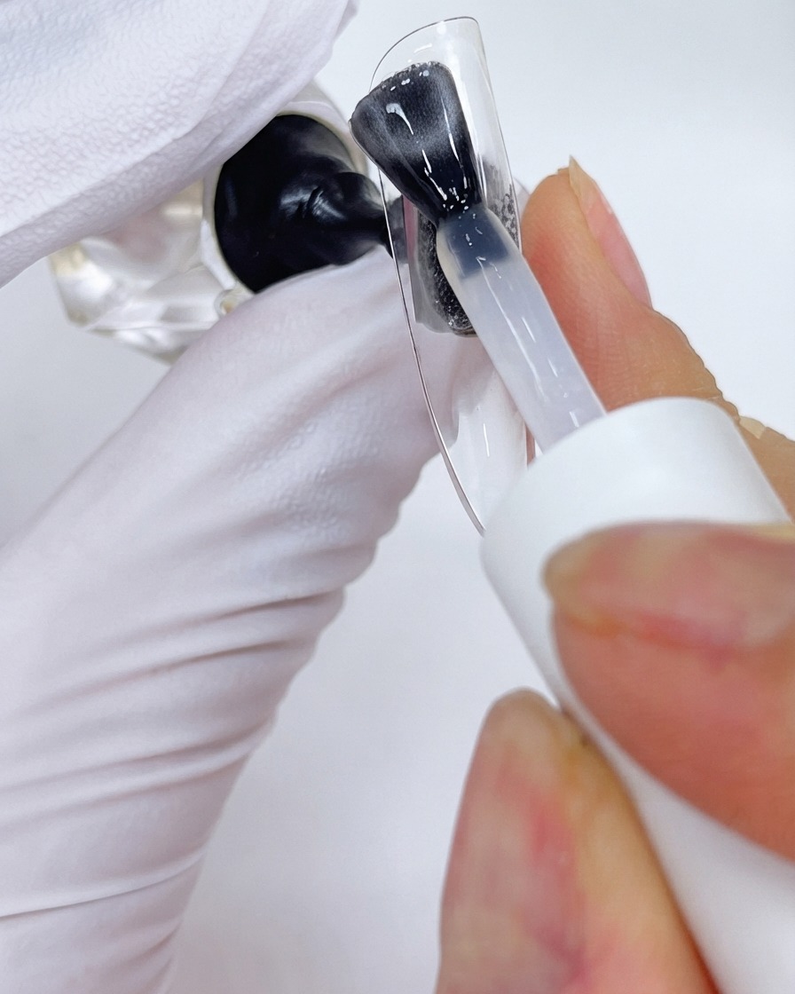 Un pennello che applica uno strato di top coat su un supporto trasparente per unghie da esposizione.