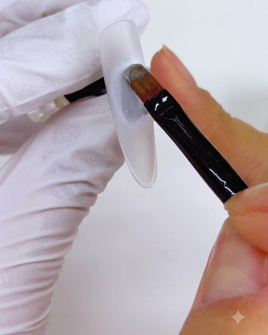Un pennello che applica uno strato di gel su una base perlata circolare su ununghia.