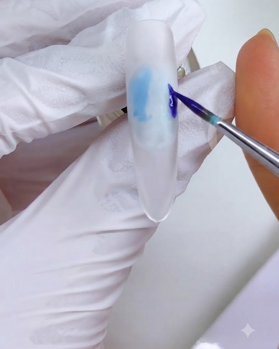 Un pennello liner fine che applica un blocco di inchiostro blu-viola sul lato destro della superficie dellunghia smerigliata bianca.