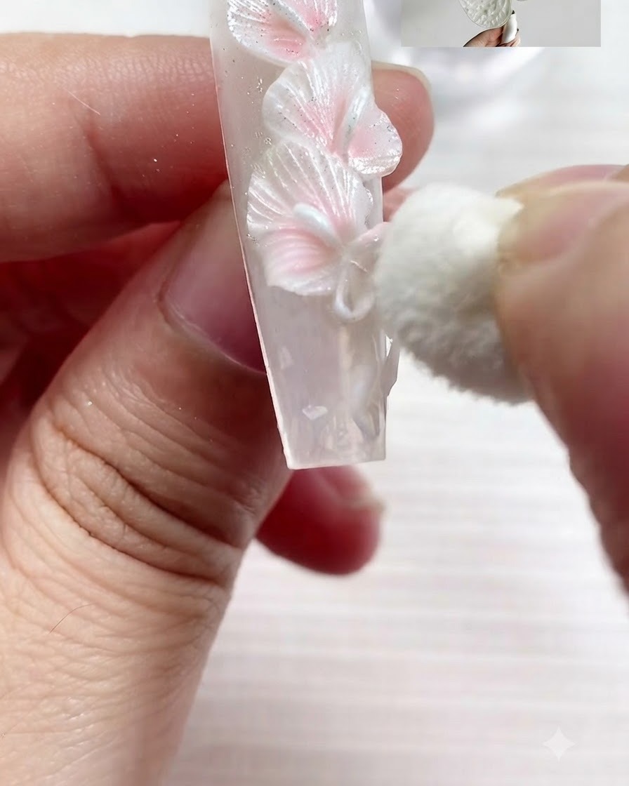Una piccola spugnetta cosmetica tampona delicatamente il pigmento bianco perla sui bordi strutturati delle calle bianche scolpite e di un fiocco su ununghia.