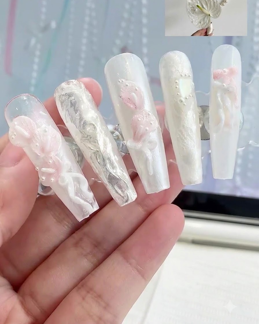 Un supporto da esposizione che sostiene diverse unghie press-on con vari design di nail art floreale 3D bianchi e rosa.
