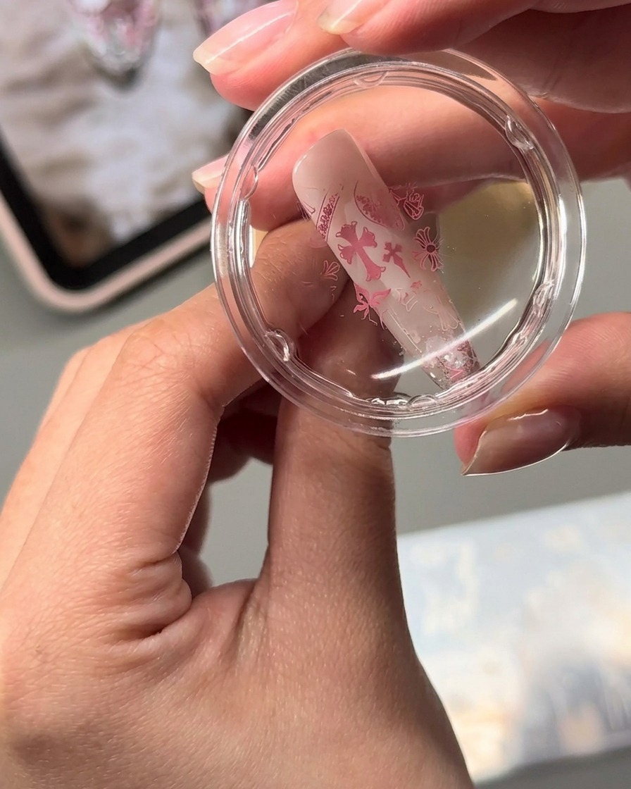 Uno stamper in gel trasparente che trasferisce disegni di nail art stampati in rosa su una superficie di unghia a mandorla.