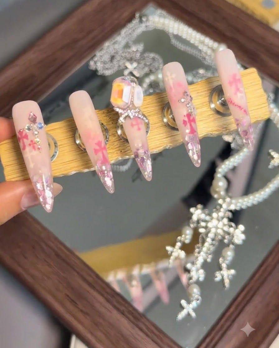 Un supporto espositivo che mostra un set di pezzi di nail art finiti con un grande cristallo prominente e un charm a fiocco sullunghia centrale.