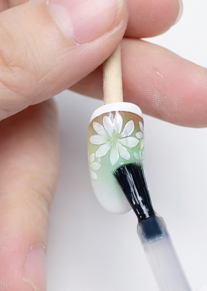 Un pennello applica il top coat opaco sopra la nail art con margherite completata.