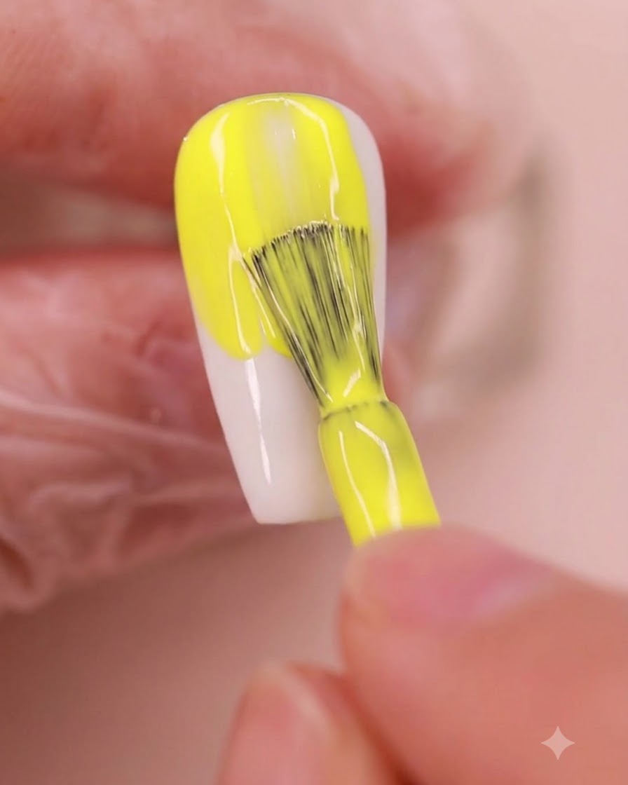 Un pennello da unghie applica uniformemente uno smalto gel giallo vibrante su ununghia a forma di mandorla.