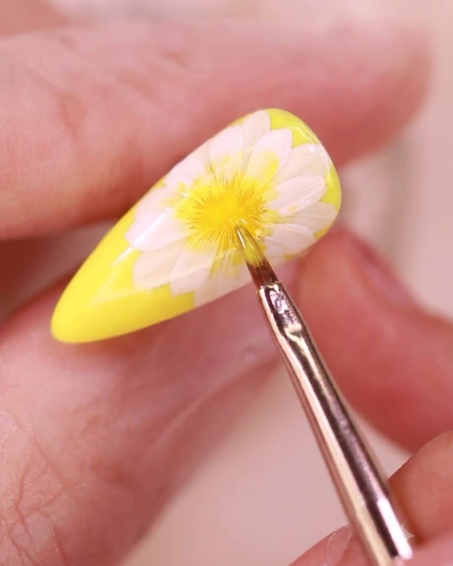 Un pennello per dettagli sottili applica un top coat trasparente su un design di unghie floreali.
