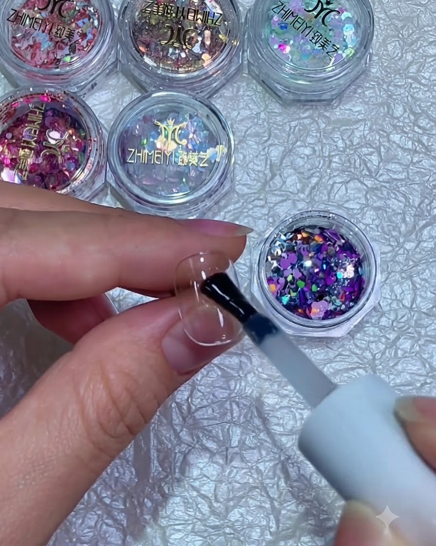 Un pennello che tiene frammenti di glitter misti viola e argento sopra ununghia coperta di gel fresco.