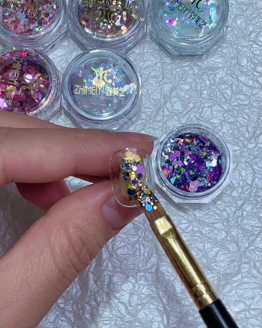 Un pennello che regola con precisione la posizione di frammenti di glitter colorati su ununghia.