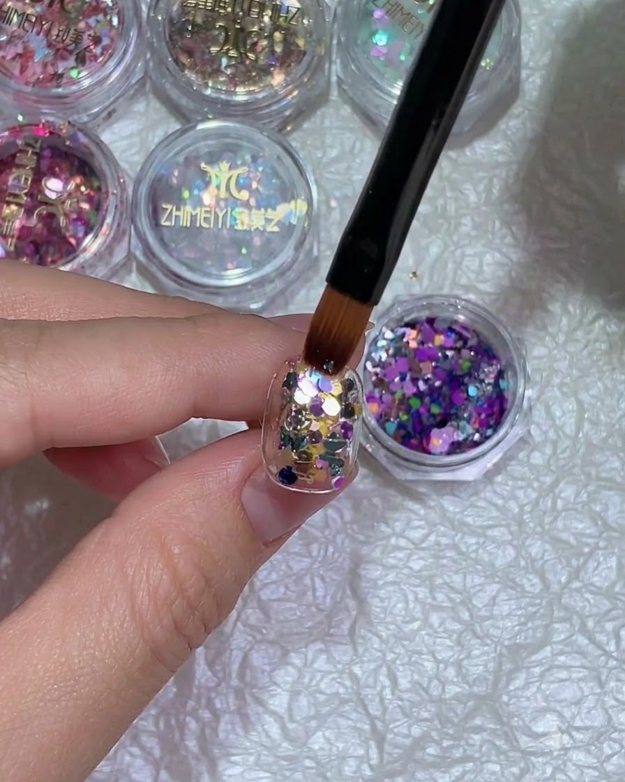 Primo piano di una mano con nail art glitterata posizionata sotto una lampada per polimerizzazione.