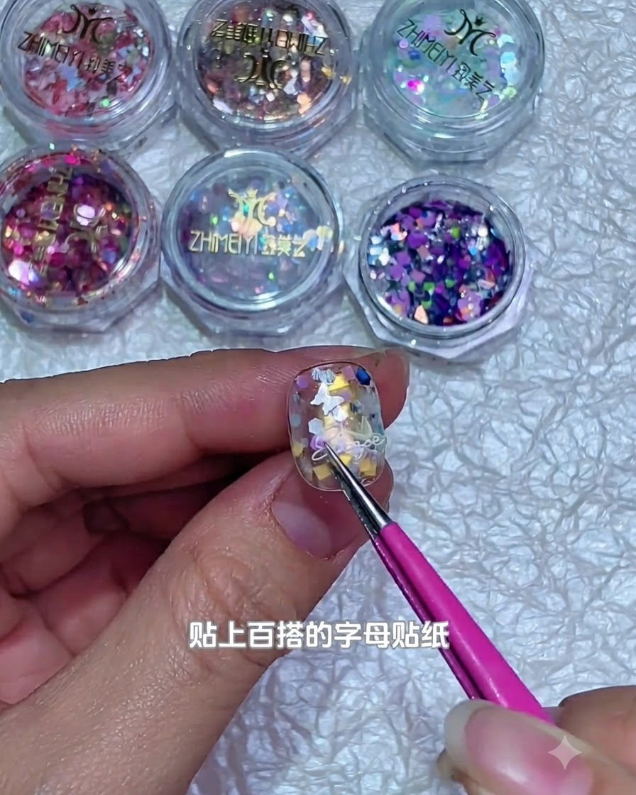 Un paio di pinzette che posizionano un minuscolo adesivo con lettera bianca sulla superficie di ununghia in gel decorata.
