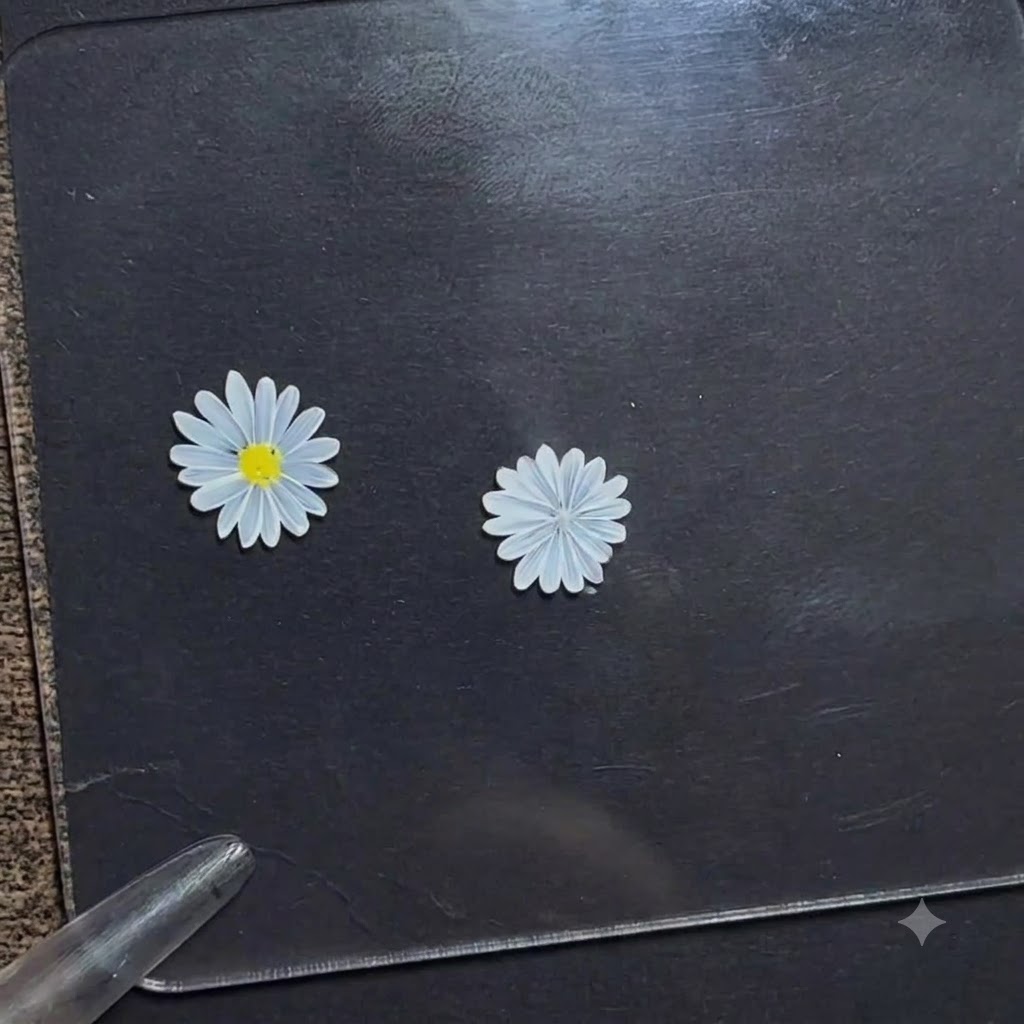 Una penna dotting che applica un piccolo punto di gel giallo brillante al centro di un fiore di margherita bianca su una tavoletta di esposizione scura.