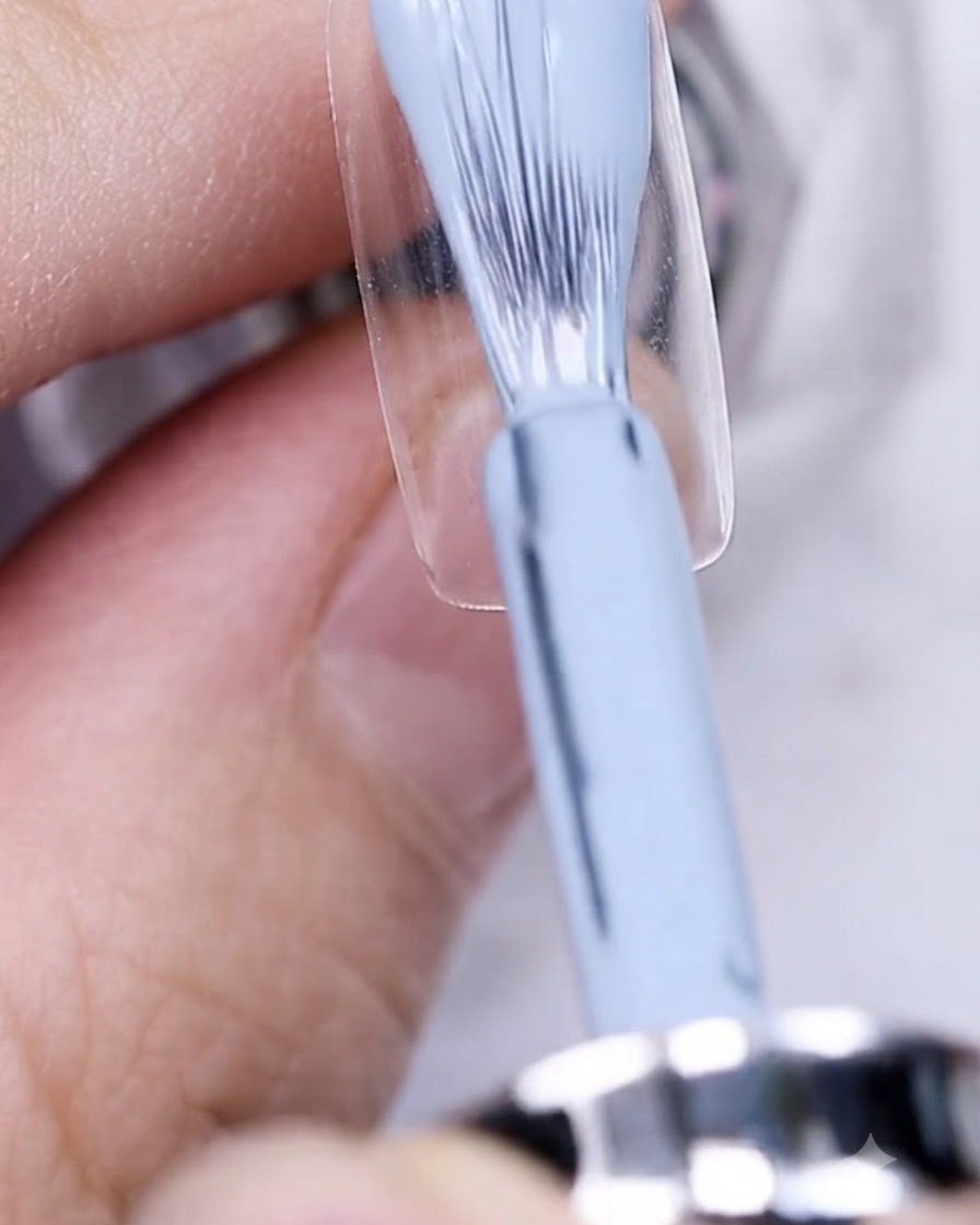 Un pennello che applica lo smalto gel grigio-blu su una piastra ungueale nuda.