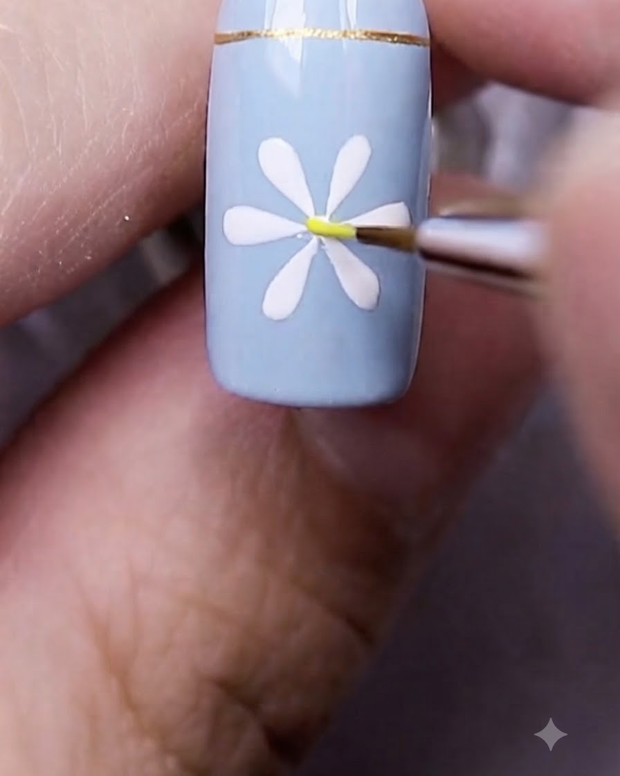 Un pennello fine per nail art che posiziona un minuscolo puntino giallo direttamente al centro della margherita bianca dipinta.