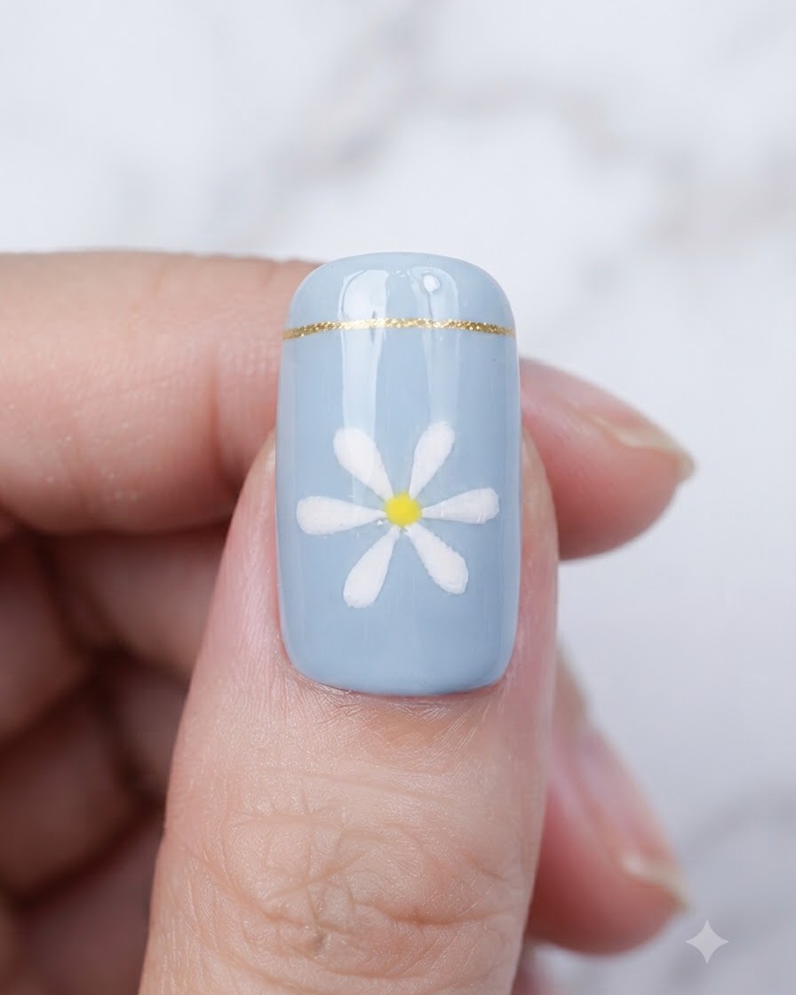 Un pennello che applica un top coat trasparente e lucido su ununghia blu finita con un design a margherita.
