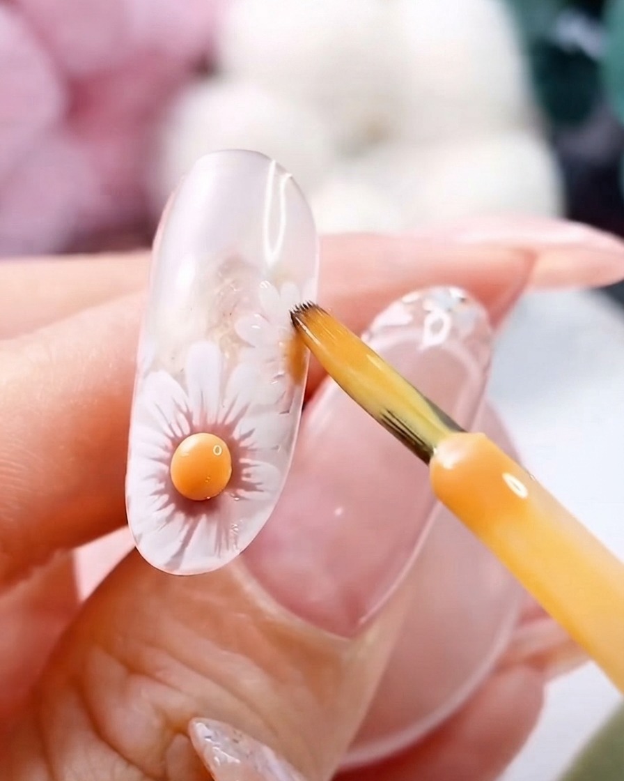 Un pennello sottile vicino a un centro di fiore giallo 3D polimerizzato su ununghia in gel trasparente.