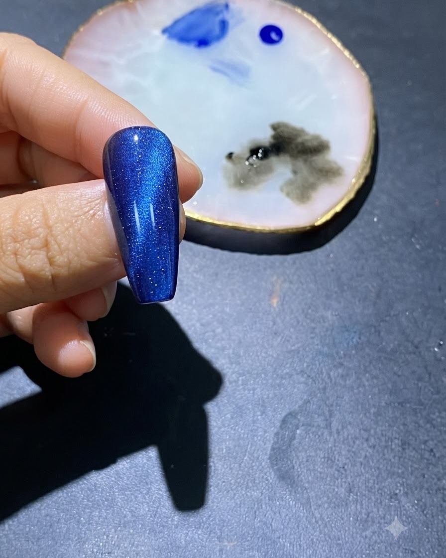 Un primo piano di ununghia in gel cat-eye blu con macchie di smalto blu al centro e una tavolozza darte vicina.