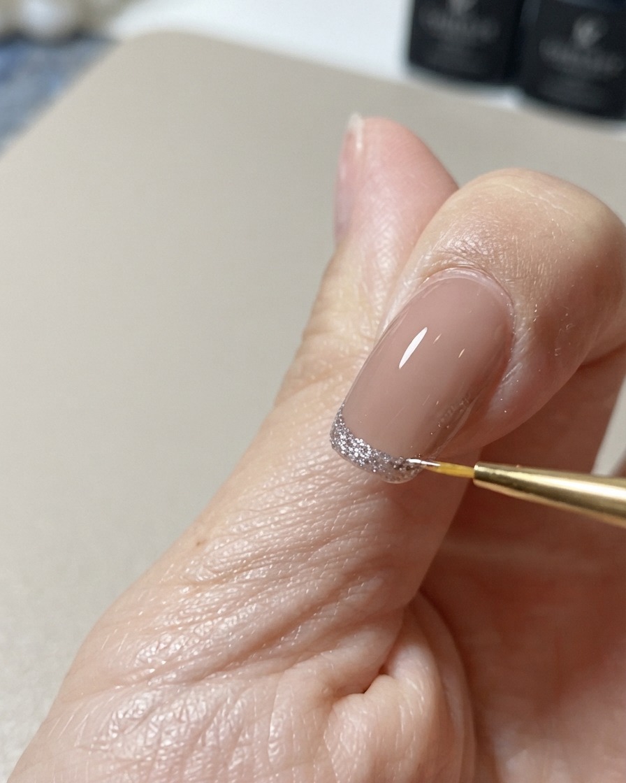 Un pennello liner fine per nail art corregge e perfeziona il bordo di una decorazione glitterata cat-eye sulla punta.