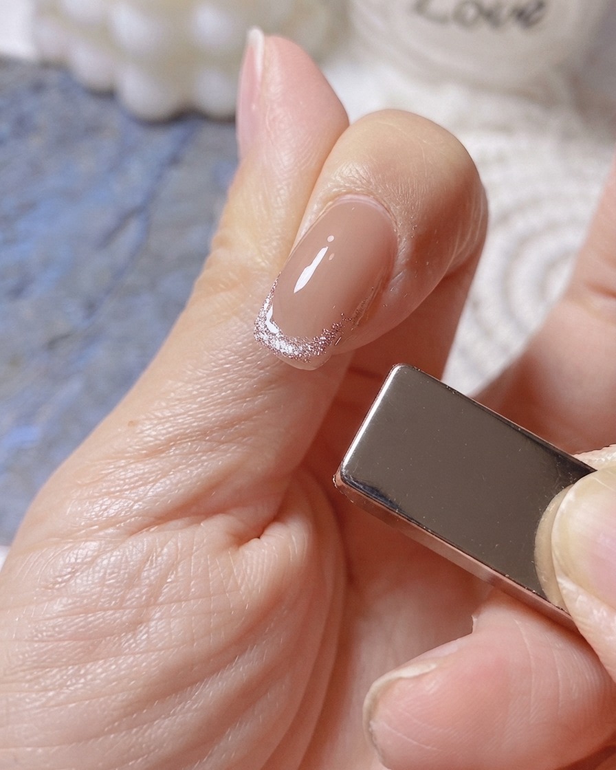 Un magnete posizionato sul lato destro di un dito per formare unampia fascia luminosa su una french tip cat-eye.