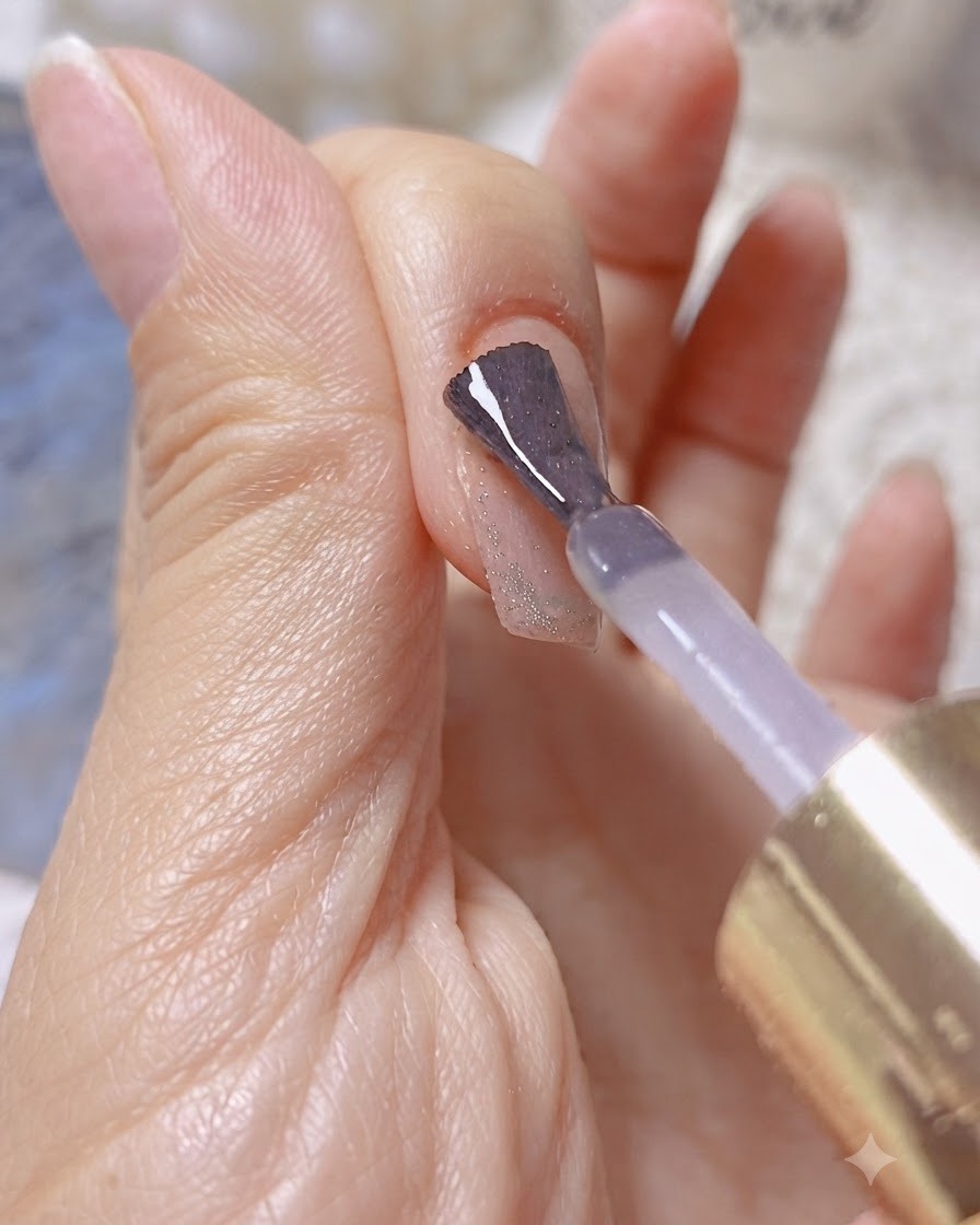 Un pennello applica un gel costruttore o rinforzante trasparente su ununghia brillante con effetto cat-eye.
