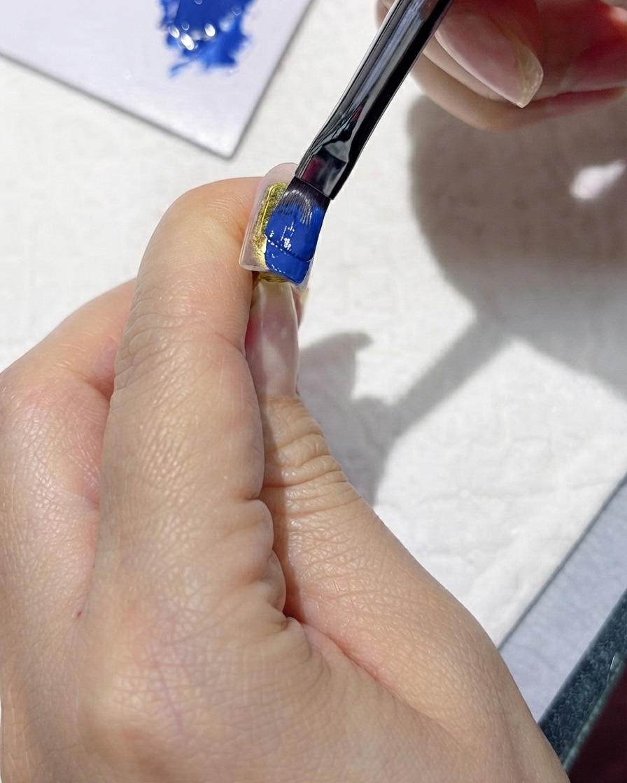 Un pennello che applica attentamente uno smalto gel blu scuro ricco su ununghia finta.