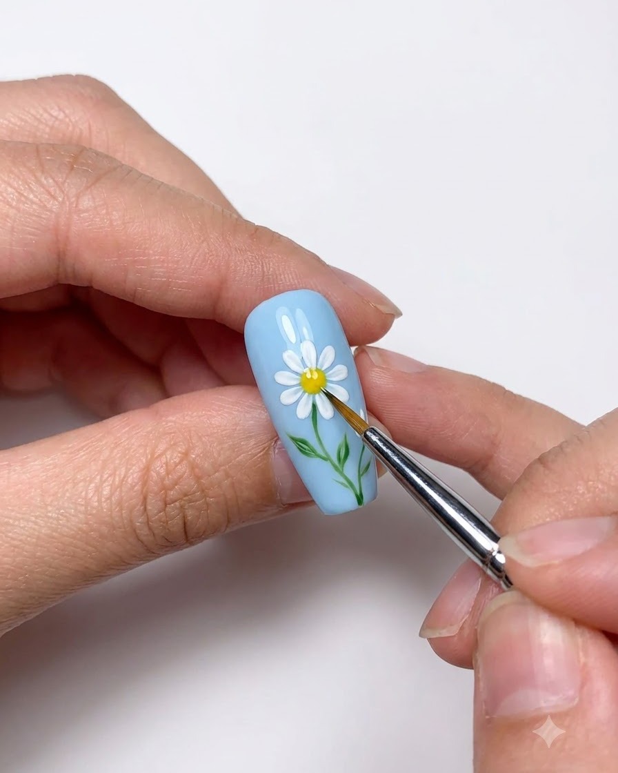 Primo piano di un dotting tool che posiziona un centro giallo sulla margherita bianca dipinta.