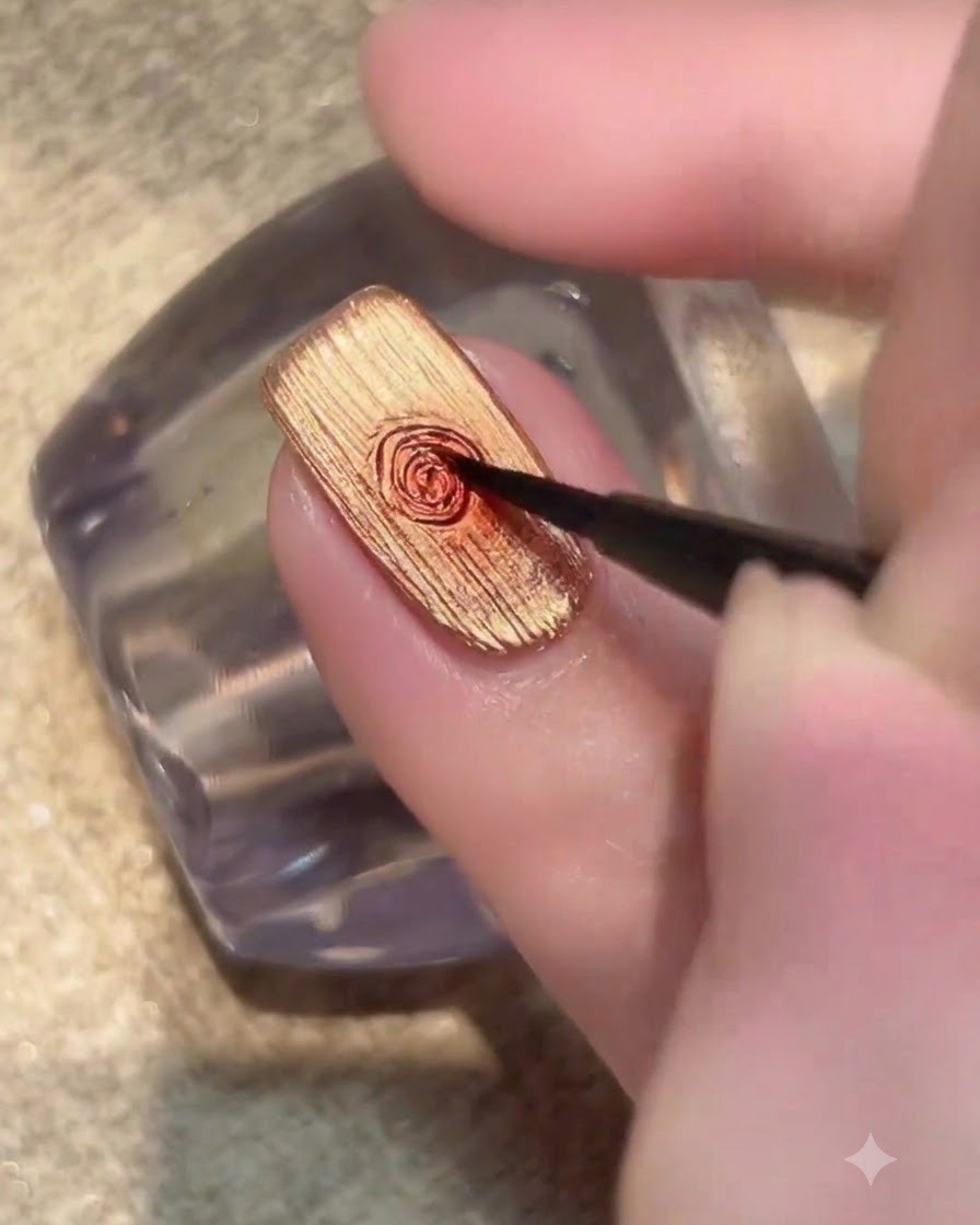 Un pennello fine che posiziona una piccola goccia di gel rosso scuro al centro di ununghia dorata.