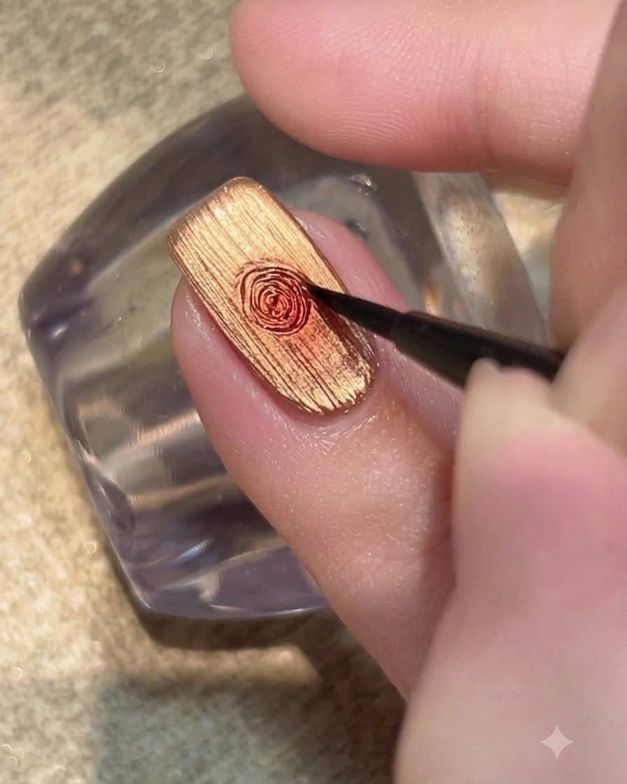 Un pennello di dettaglio fine che sfuma una goccia di gel rosso in un motivo floreale a rosa circolare su ununghia color oro metallizzato.